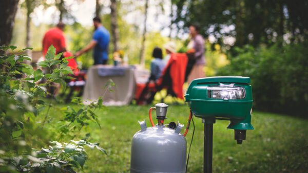 Mosquito Magnet hyttysansa pihalla. Taustalla seurue grillaamassa.